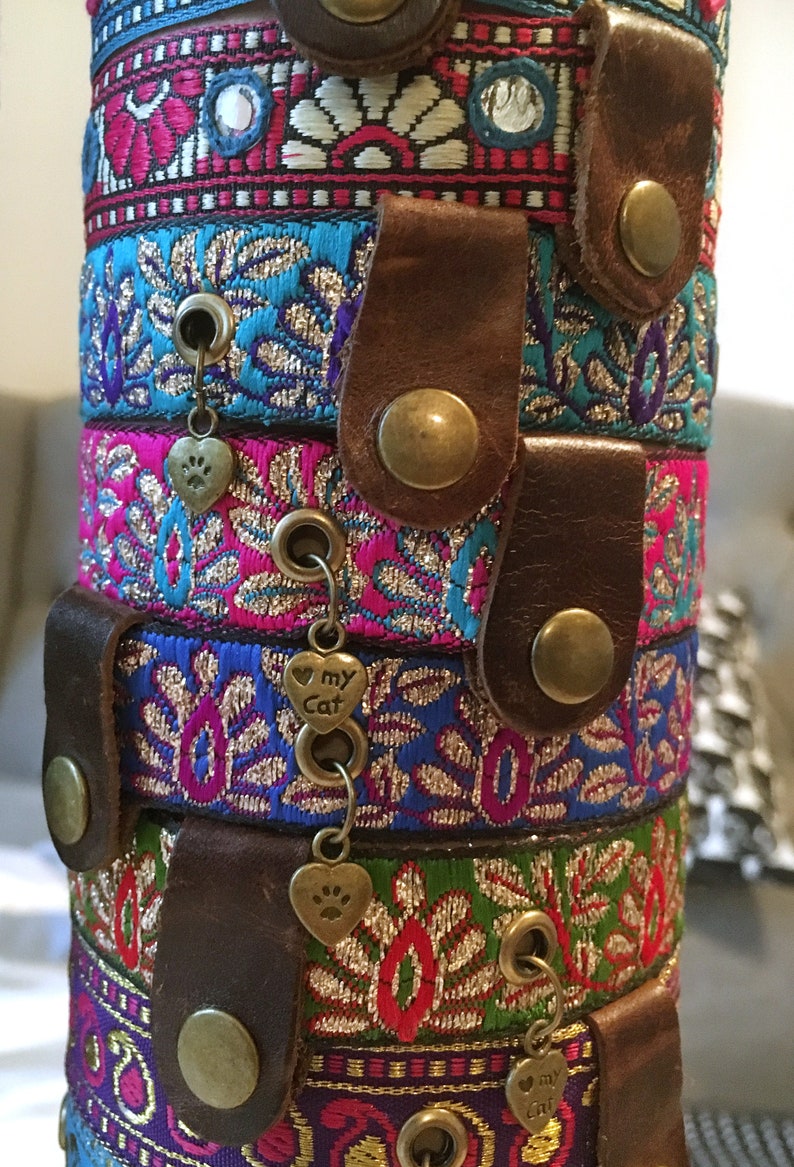 May include: A stack of colorful, patterned cat collars with leather accents and metal charms. The charms feature paw prints and the words "my cat".