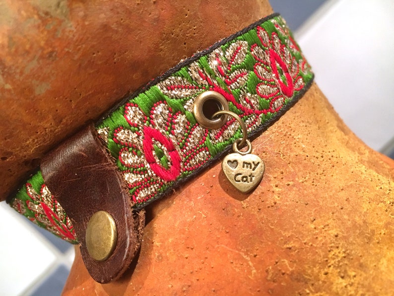 May include: A green, red, and gold patterned cat collar with a brown leather buckle and a heart-shaped charm that says "I love my cat".