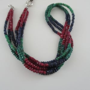 Könnte beinhalten: Eine mehrreihige Halskette aus roten, grünen und blauen Edelsteinperlen. Die Halskette besteht aus mehreren Perlenreihen, wobei jede Reihe eine andere Farbe von Edelsteinen aufweist.