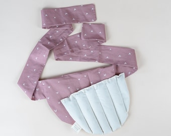 Pode incluir: Um envoltório de tecido rosa com um padrão de corações brancos e um inserto acolchoado branco. O envoltório é amarrado em torno do inserto, que tem a forma de uma lua crescente.