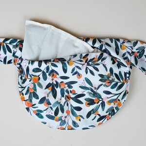 Könnte beinhalten: Eine weiße Stofftasche mit einem Blumendruck mit Orangenblüten, grünen Blättern und weißen Blüten. Die Tasche ist offen und das Futter ist sichtbar.