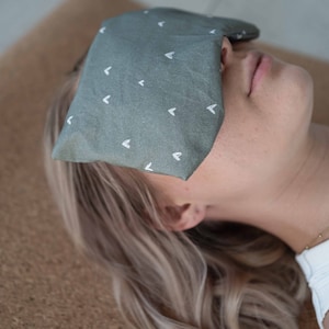 Può includere: Una persona indossa una maschera per gli occhi verde con motivi a forma di cuore bianchi. La maschera copre i suoi occhi e la persona è sdraiata su una superficie marrone.