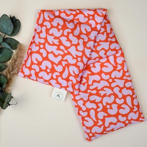 May include: A pink and orange fabric hot water bottle with a white label that says "of" and a pair of scissors.