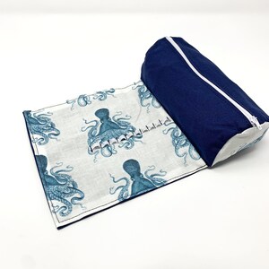 Pode incluir: Uma bolsa azul com z&iacute;per com um forro de tecido branco que apresenta um padr&atilde;o repetido de ilustra&ccedil;&otilde;es de polvos azuis. A bolsa est&aacute; aberta e desenrolada, revelando o forro.