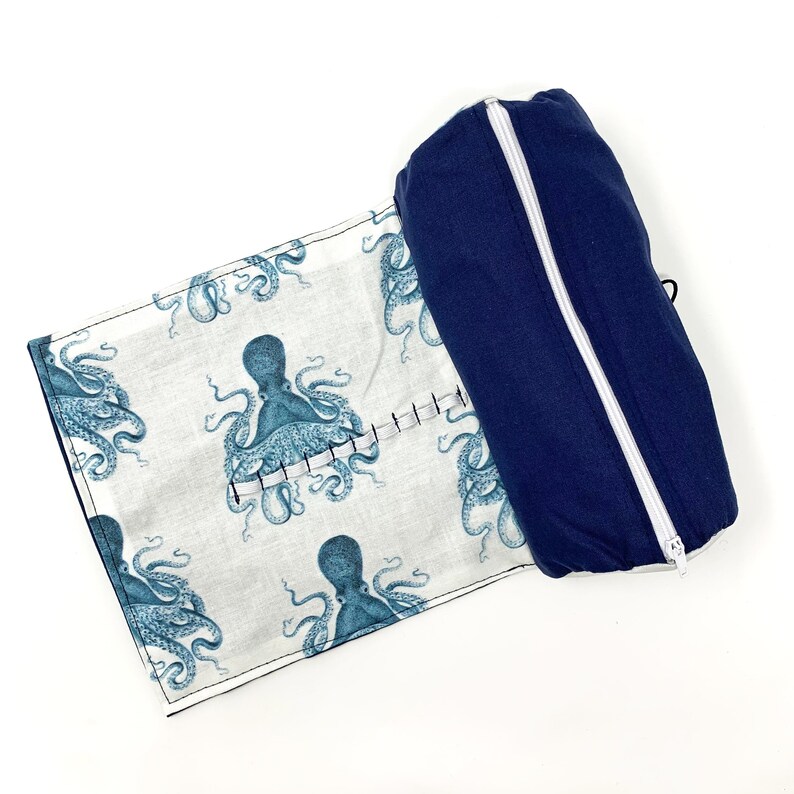 Pode incluir: Uma bolsa azul com z&iacute;per branco. A bolsa est&aacute; aberta e dobrada para tr&aacute;s para revelar um tecido branco com um padr&atilde;o repetido de ilustra&ccedil;&otilde;es de polvo azuis.