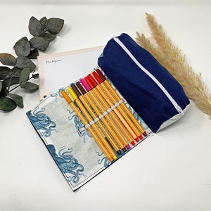 Pode incluir: Um estojo de l&aacute;pis azul com um z&iacute;per branco e um forro de estampa de polvo branco e azul. O estojo est&aacute; aberto e cheio de marcadores coloridos.
