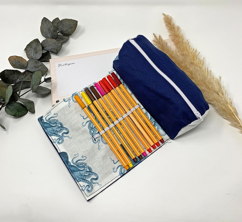 Pode incluir: Um estojo de l&aacute;pis azul com um z&iacute;per branco e um forro de estampa de polvo branco e azul. O estojo est&aacute; aberto e cheio de marcadores coloridos.
