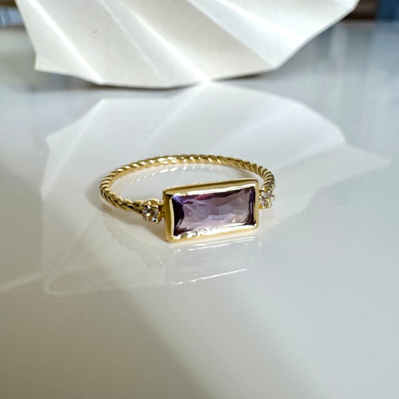 May include: A gold ring with a rectangular amethyst gemstone and two small diamond accents.