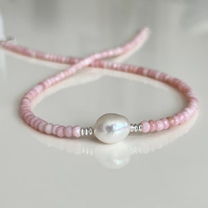 May include: A delicate pink gemstone necklace with a single large white pearl pendant. The necklace is made with small, faceted beads and silver accents.