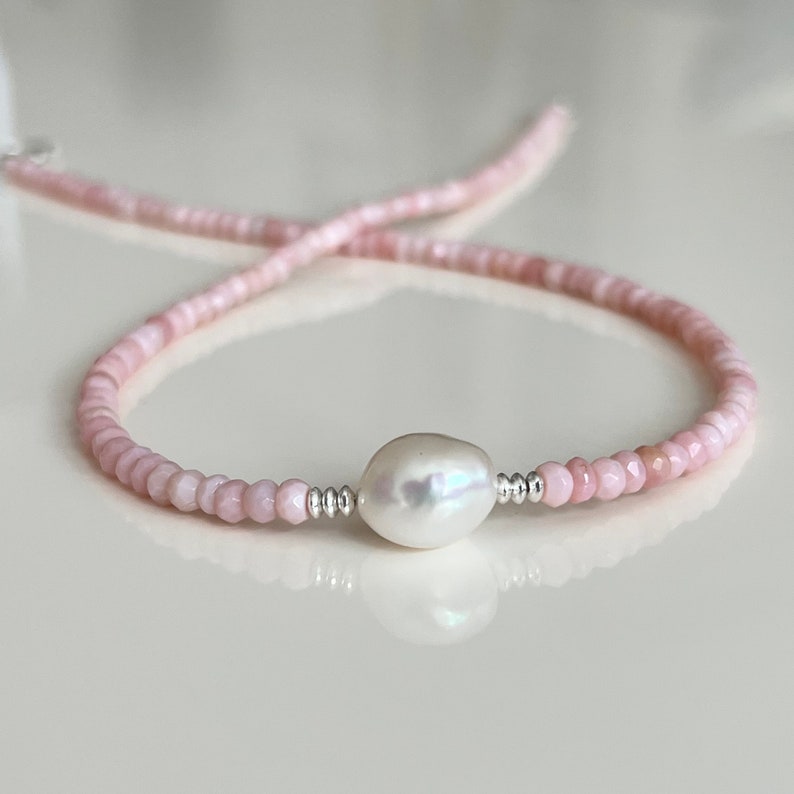 May include: A delicate pink gemstone necklace with a single large white pearl pendant. The necklace is made with small, faceted beads and silver accents.