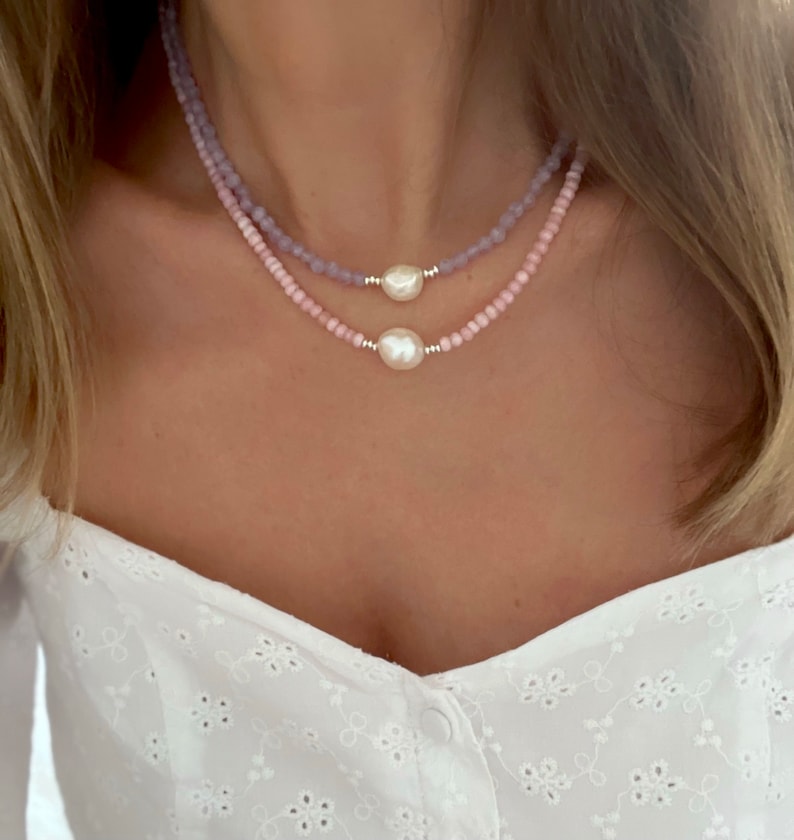 May include: Two layered necklaces with pink and purple beads and a pearl pendant.
