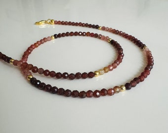 Op de afbeelding: Een gelaagde ketting gemaakt van kleine, gefacetteerde, roodbruine kralen met gouden accenten.