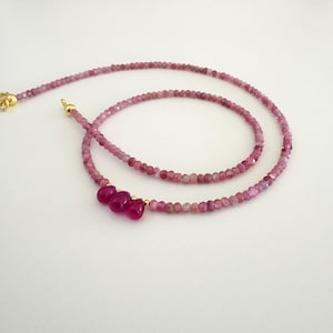 Peut inclure: Un collier délicat en pierres précieuses roses avec trois pierres précieuses roses plus grandes suspendues au centre. Le collier est fait de petites perles rondes et a un fermoir en or.