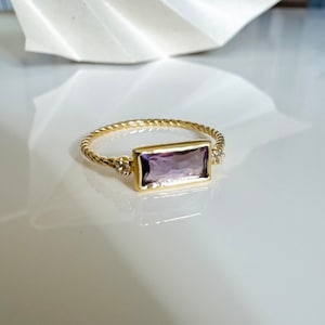 May include: A gold ring with a rectangular amethyst gemstone and two small diamond accents. The ring has a twisted band.