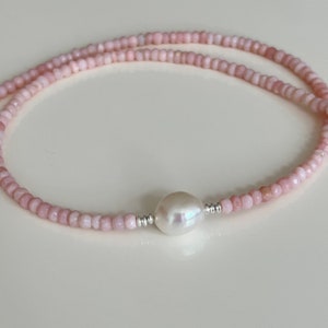 May include: A delicate pink gemstone necklace with a single large white pearl pendant. The necklace is made of small, evenly spaced beads.