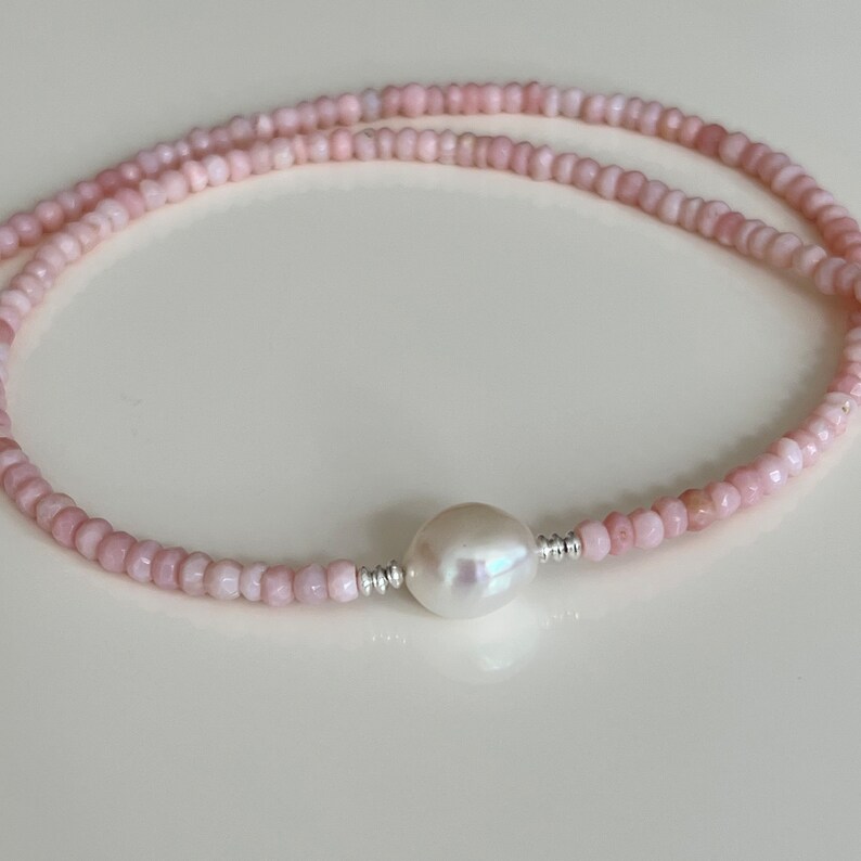 May include: A delicate pink gemstone necklace with a single large white pearl pendant. The necklace is made of small, evenly spaced beads.