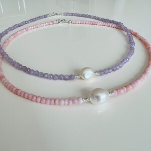 May include: Two delicate necklaces with a pearl accent. The top necklace is made of light purple beads and the bottom necklace is made of light pink beads.