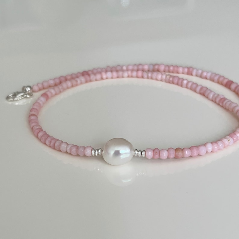 May include: A delicate pink gemstone necklace with a single white pearl pendant. The necklace is made of small, faceted beads and is strung on a silver chain.