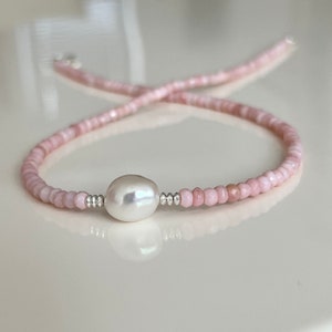 May include: A delicate pink beaded bracelet with a single large white pearl in the center.