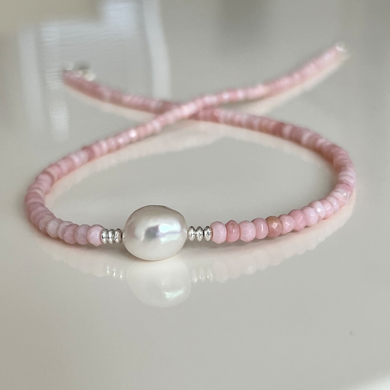 May include: A delicate pink beaded bracelet with a single large white pearl in the center.