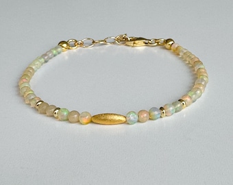 Pode incluir: Um delicado bracelete de ouro com um único acento de barra de ouro e contas de opala iridescente.