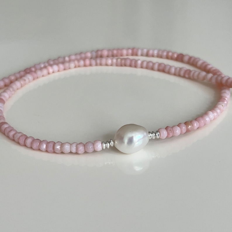 May include: A delicate pink beaded necklace with a single large white pearl pendant.