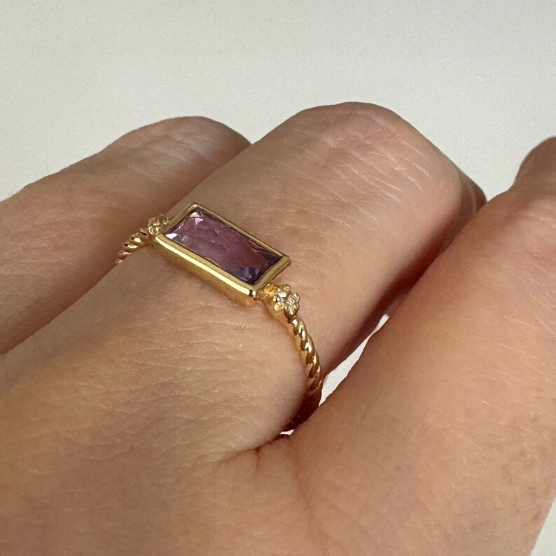 May include: A gold ring with a purple rectangular gemstone and small clear stones on the band.