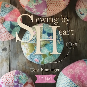 Könnte beinhalten: Eine Sammlung bunter Patchwork-Stoffkürbisse. Das Bild zeigt den Text "Sewing by Heart" und den Namen des Autors, Tone Finnanger, sowie das "Tilda"-Logo. Die Kürbisse sind aus verschiedenen floralen und gemusterten Stoffen gefertigt.