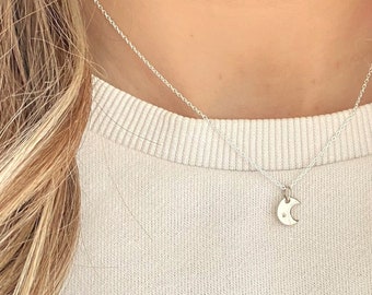 May include: A silver chain necklace with a small crescent moon pendant. The moon has a small star in the center.