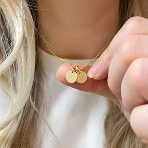 May include: A gold chain necklace with two small round gold charms. The charms are engraved with the letters "M" and "H".