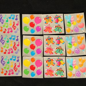May include: A sheet of colorful stickers featuring musical notes, balloons, and clowns. The stickers are on a white background.