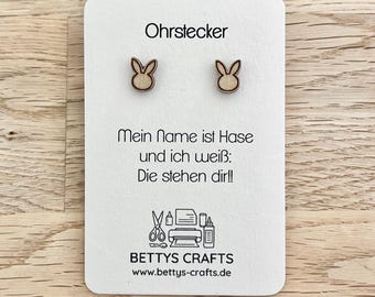 Puede incluir: Pendientes de botón de madera con forma de conejito, presentados en una tarjeta blanca. La tarjeta tiene texto en alemán, incluyendo "Ohrstecker" y "Mein Name ist Hase". Los pendientes son de color marrón claro. La tarjeta muestra el logo y el sitio web de "BETTYS CRAFTS".