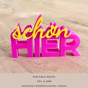 Könnte beinhalten: Ein leuchtend pinkfarbenes 3D-gedrucktes Schild mit der Aufschrift "schön HIER". Das Wort "schön" ist gelb, was einen Kontrast erzeugt. Das Schild steht auf einer hellbraunen Holzoberfläche. Ein dekorativer Artikel.