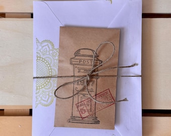 May include: A white envelope with a gold floral design on the left side, holding a brown paper card tied with twine. The card features a vintage post office illustration with the text "POST" and "1977". A red stamp is also visible.