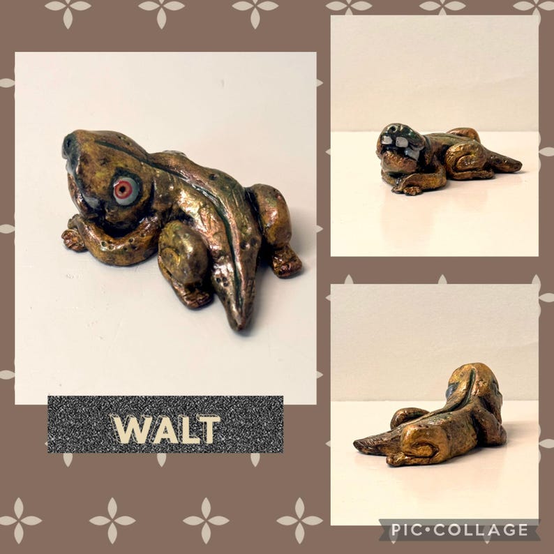 May include: A handcrafted, bronze-colored frog figurine with red eyes. The frog is in a resting pose, with detailed texture and a metallic finish. The name "WALT" is displayed on a rectangular label below the frog.