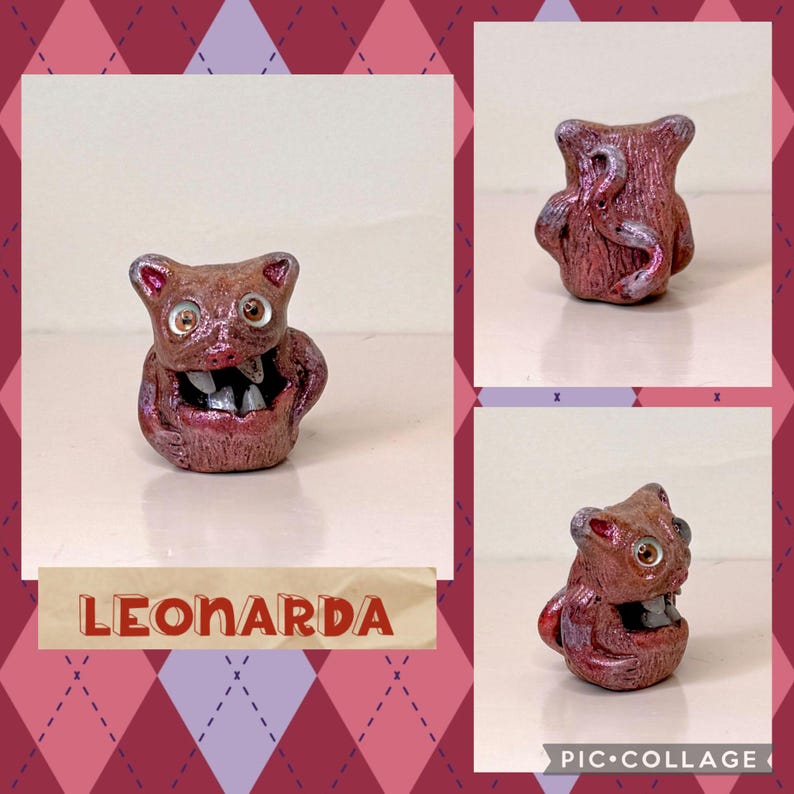 May include: A handmade, reddish-brown ceramic figurine with a wide open mouth revealing teeth. The figurine has large, round eyes and is labeled "LEONARDA" in a banner. The background is a collage with a diamond pattern.
