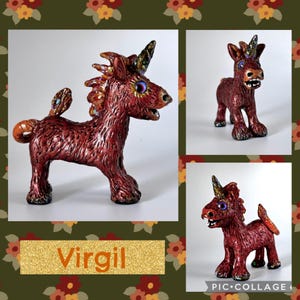 May include: A handcrafted, red-brown unicorn figurine with a textured surface, a spiraled horn, and iridescent accents. The figurine has a whimsical design with large eyes and a curled tail. The name "Virgil" is displayed on a gold glitter background.
