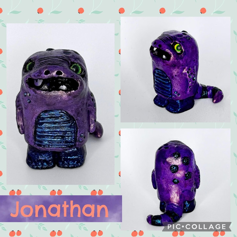 May include: A handcrafted purple monster figurine with green eyes, a toothy grin, and a blue belly. The figurine is painted with metallic accents and has a small tail. The name "Jonathan" is written on a purple banner below the figurine.