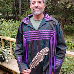 Puede incluir: Una persona vistiendo una camisa de patrón verde oscuro, azul y morado con ribetes de cinta morada y una pluma en la mano.