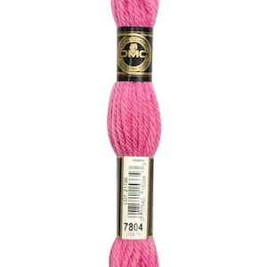 May include: A pink skein of DMC tapestry wool with a black and gold label that reads "Laine Colbert DMC Tapestry Wool" and includes the lot number 21786 and the product number 7804.