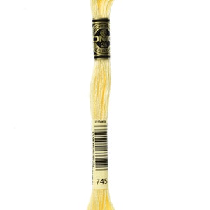 May include: A skein of DMC embroidery floss in colour 745, a pale yellow. The floss is wound around a cardboard spool with a black and gold label that reads "Mouline Special DMC 25 8 m (8.7 yd) 3915045V".