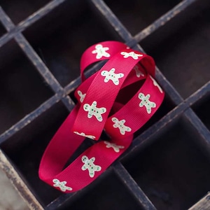 May include: A red ribbon with white gingerbread men printed on it is coiled in a wooden box with multiple compartments.
