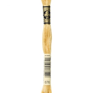 May include: A spool of DMC embroidery floss in colour 676, a pale yellow. The spool is labelled with the DMC logo and the number 25, indicating the length of the floss. The label also includes the text "Outline Special" and a barcode.