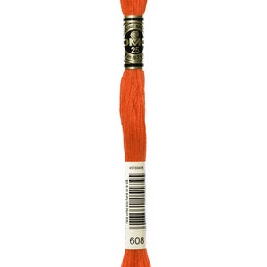 May include: A vibrant orange embroidery thread spool. The label displays "DMC 25" and the colour code "608". The thread is tightly wound, suitable for embroidery and other crafts. The label also includes a barcode and text in Spanish.