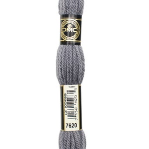 May include: A skein of DMC Tapestry Wool yarn in a muted grey colour, labelled with the number 7620. The label features the DMC logo and product information. The yarn is tightly wound, showing its texture.
