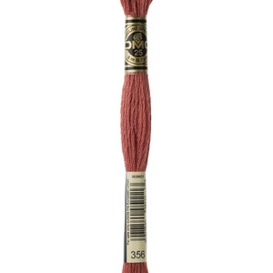 May include: A spool of DMC embroidery floss in colour 356, a deep reddish-brown shade. The spool is labelled with the DMC logo and the number 25, indicating the length of the floss. The label also includes the text "Mouline Special" and "8 m (8.7 yds)".