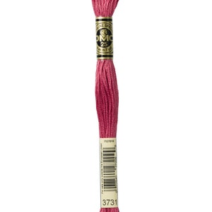 May include: A spool of DMC embroidery floss in colour 3731, a deep pink shade. The spool is labelled with the DMC logo and the colour number. The floss is 8.7 yards (3 metres) long.