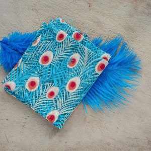 May include: A folded blue fabric with a white and red peacock feather pattern. The fabric is surrounded by two blue feathers.