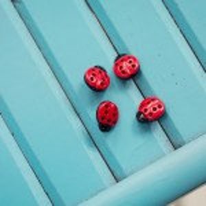May include: Four red ladybug-shaped buttons with black spots on a blue wooden surface.