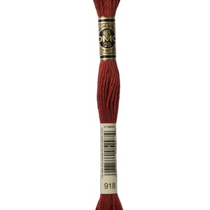 May include: A spool of DMC embroidery floss in colour 918, a deep reddish-brown. The spool is labelled with the DMC logo and the number 25, indicating the length of the floss.